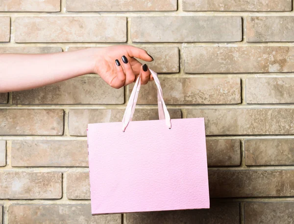 Saco de compras rosa claro na mão feminina na parede de tijolo — Fotografia de Stock