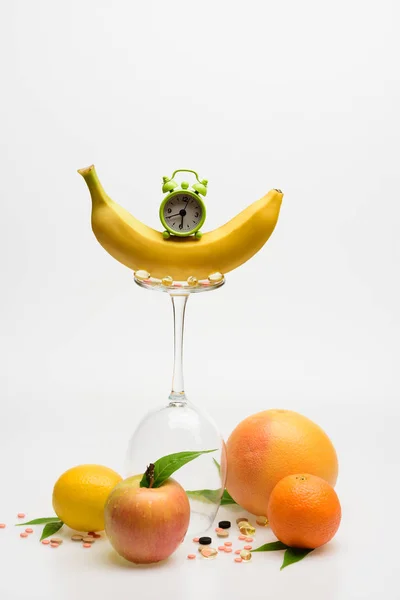 Orange, bananer, grapefrukt, äpple, citron, vinglas med piller, kapsel, klocka — Stockfoto
