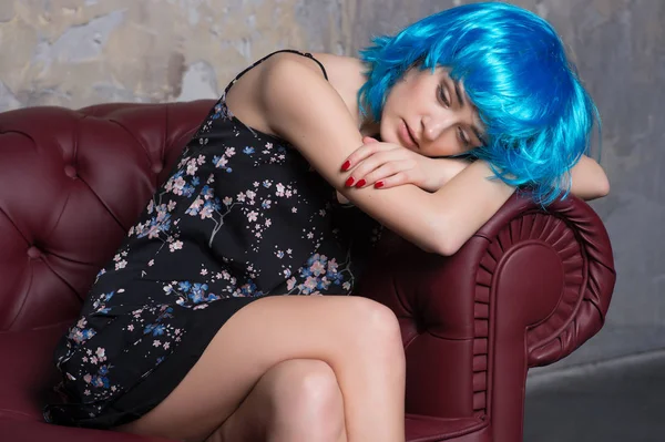 Bonita chica en peluca azul relajarse en sofá de cuero marrón —  Fotos de Stock