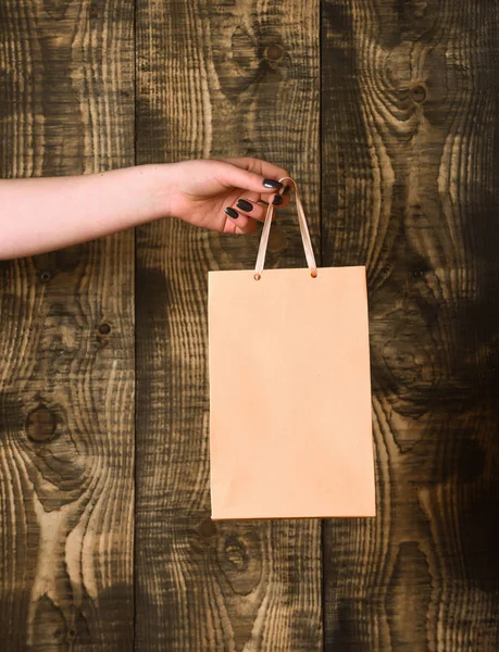 Saco de compras laranja claro na mão feminina no fundo de madeira — Fotografia de Stock