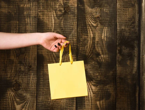 나무 배경에 여성 손에 노란 쇼핑백 — 스톡 사진