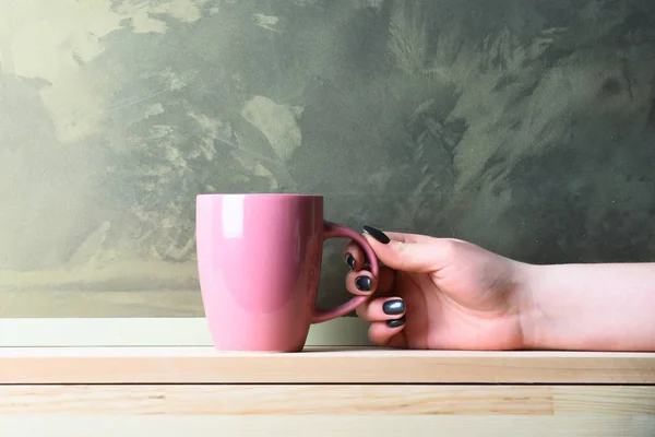 pink tea or coffee cup in hand on grey background