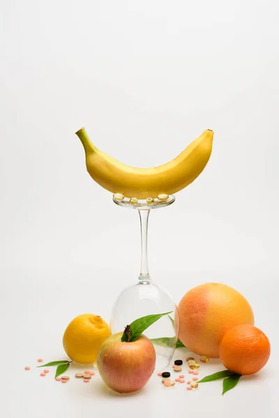 Orange, bananer, grapefrukt, äpple, citron, vinglas med piller och kapsel — Stockfoto