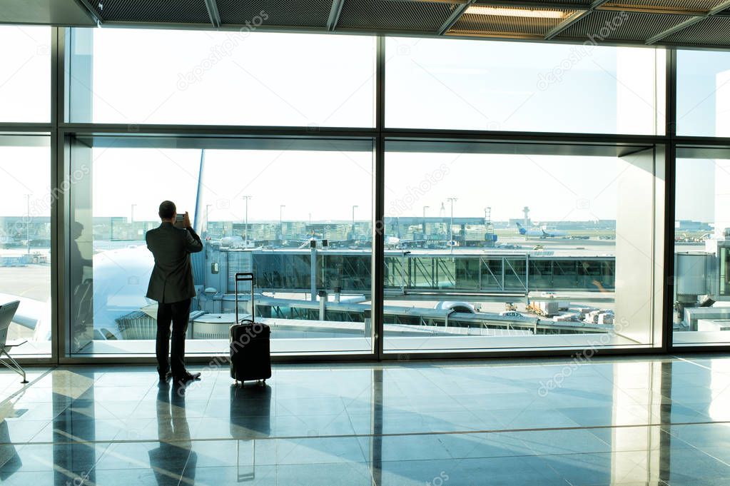 man with luggage waiting hall of airport at window glass