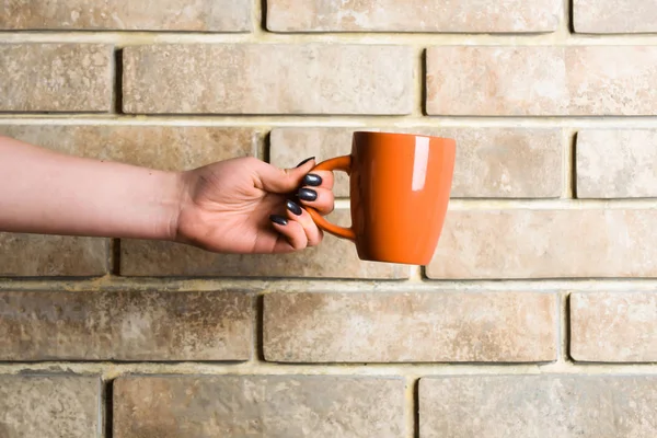 Té naranja o taza de café en la mano en la pared de ladrillo — Foto de Stock