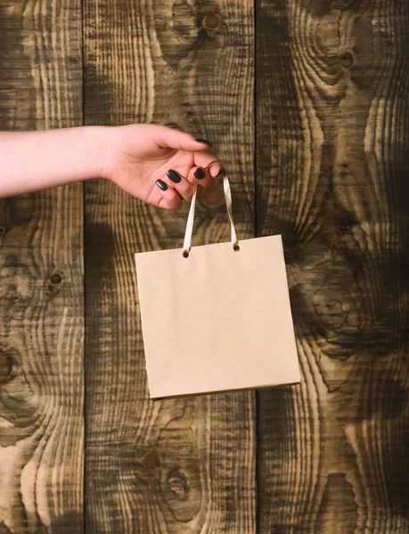 Saco de compras cinza marrom na mão feminina no fundo de madeira — Fotografia de Stock