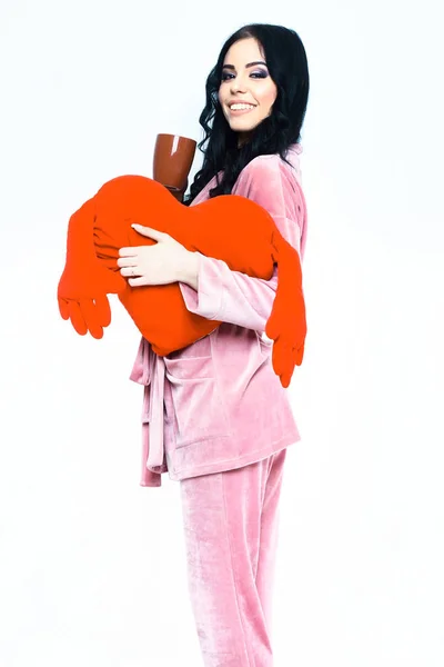 Menina sorridente em terno casa veludo rosa com coração de travesseiro — Fotografia de Stock