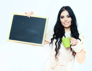 Bej bornozlu gülümseyen kız tahta ve kupa tutuyor.