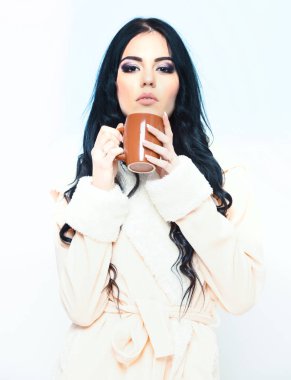 Bej renkli kadife bornoz giyen seksi kız elinde bardak tutuyor.