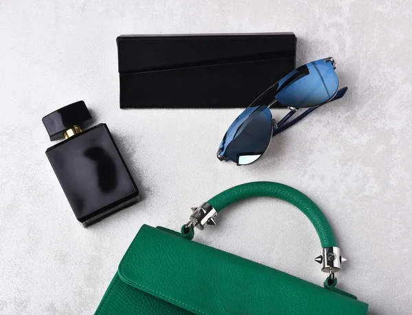 small womans leather green bag with sunglasses, perfume and case