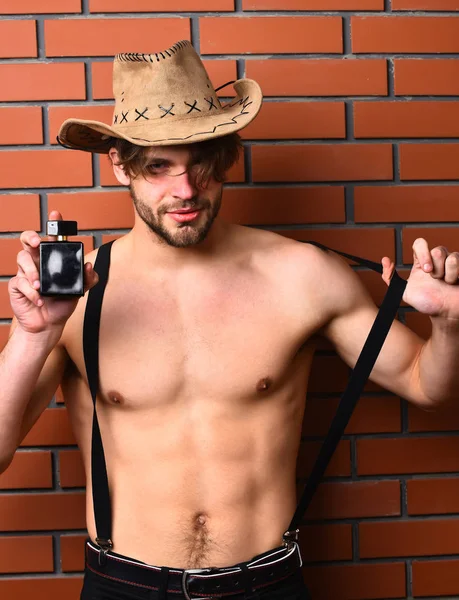 Caucasian bearded sexy macho man in cowboy hat holding perfume — Stock Photo, Image