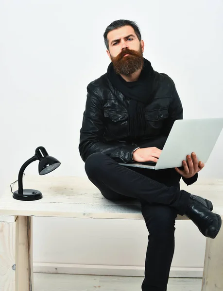 Barbudo brutal caucásico hipster sentado en la mesa con el ordenador portátil — Foto de Stock