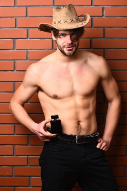 Beyaz sakallı seksi maço kovboy şapkalı adam parfüm tutuyor.