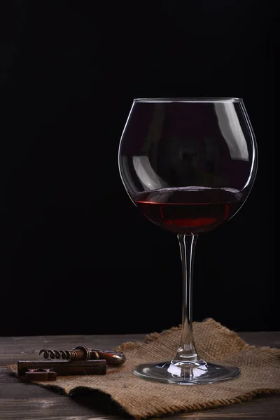 Wineglass with wine, corkscrew on wooden table with sackcloth napkin — Stock Photo, Image