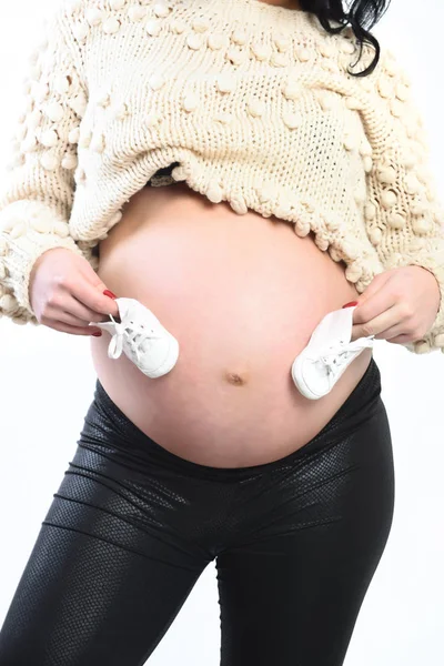Женские руки беременной женщины, держащей детские сапоги на животе — стоковое фото