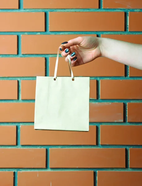 Saco de compras branco na mão feminina na parede de tijolo — Fotografia de Stock