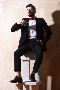 Sakallı adamın elinde matara, stüdyo duvarında ciddi bir yüz var.