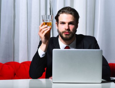 Sakallı adam, elinde bir bardak viski tutan iş adamı dizüstü bilgisayarda çalışıyor.