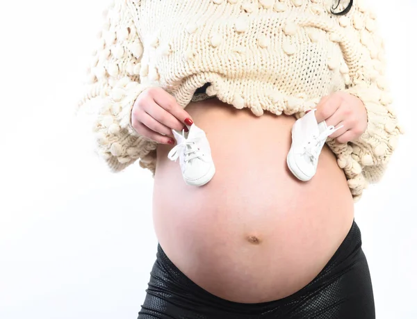 Mãos femininas de mulher grávida segurando botas de bebê na barriga — Fotografia de Stock