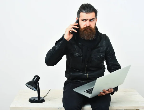 Bearded brutal caucasian hipster sitting on table with laptop — Stock Photo, Image