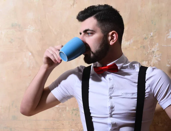 bearded man drinking coffee, tea from cup with serious face