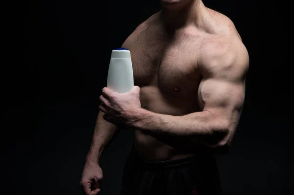 Bello bodybuilder uomo con il corpo muscolare tiene bottiglia shampoo — Foto Stock