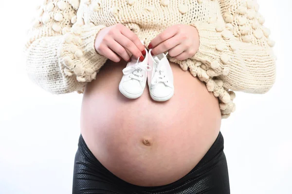 Manos femeninas de mujer embarazada sosteniendo botines de bebé en el vientre — Foto de Stock