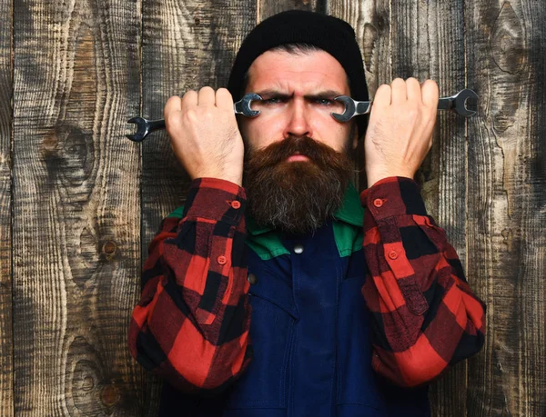 Bearded brutal caucasian mechanic holding metallic wrenches