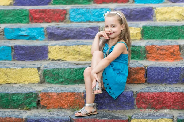 Malá usměvavá holčička v modrých šatech na barevné schody — Stock fotografie