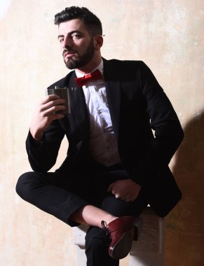 Sakallı adamın elinde matara, stüdyo duvarında ciddi bir yüz var.