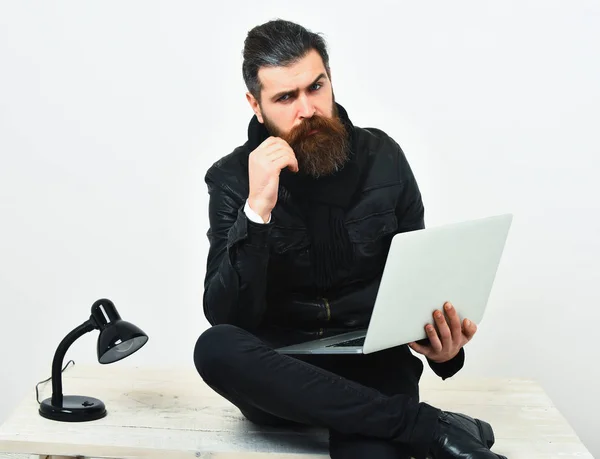 Bearded brutal caucasian hipster sitting on table with laptop — Stock Photo, Image