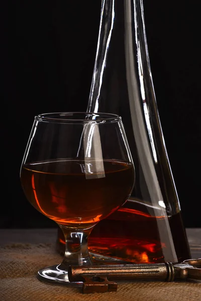 Glass, carafe with cognac, whiskey and key on wooden table — Stock Photo, Image