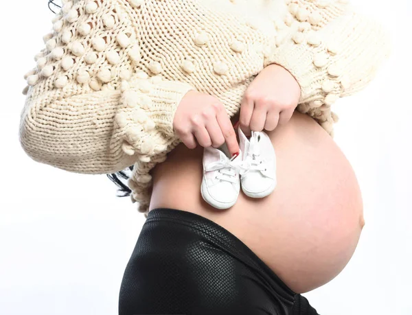 Les mains féminines de la femme enceinte tenant des chaussons de bébé sur le ventre — Photo