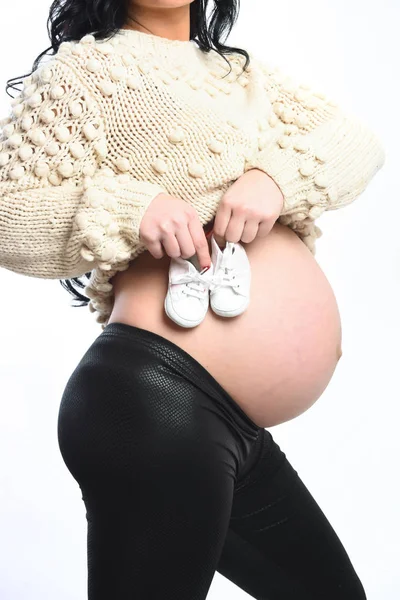 Manos femeninas de mujer embarazada sosteniendo botines de bebé en el vientre —  Fotos de Stock