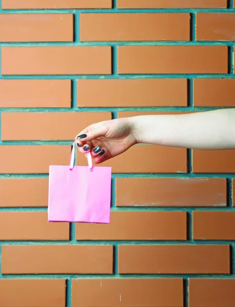 Saco de compras rosa na mão feminina na parede de tijolo — Fotografia de Stock