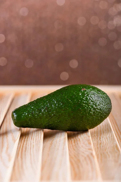 Frische grüne Avocado auf braunem Holztisch, prickelnder Hintergrund — Stockfoto