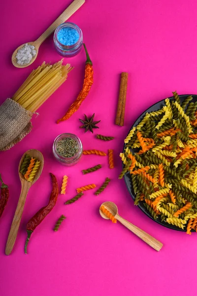 Pasta fusilli secca colorata su piatto nero e grappolo di spaghetti — Foto Stock