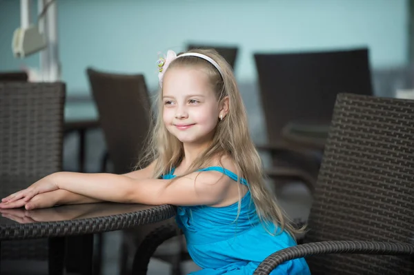 Pequeña niña sonriente en vestido azul cerca de la mesa de café —  Fotos de Stock