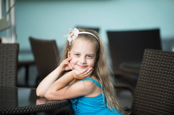 Pequeña niña sonriente en vestido azul cerca de la mesa de café —  Fotos de Stock