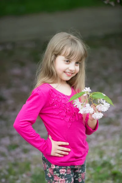 Liten flicka med leende ansikte holding rosa sakura blossom — Stockfoto