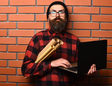 Kaba sakallı, beyaz tenli hippi elinde dizüstü bilgisayar ve el işi kâğıdı tutuyor.