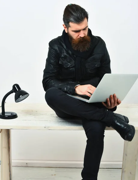 Barbudo brutal caucásico hipster sentado en la mesa con el ordenador portátil — Foto de Stock