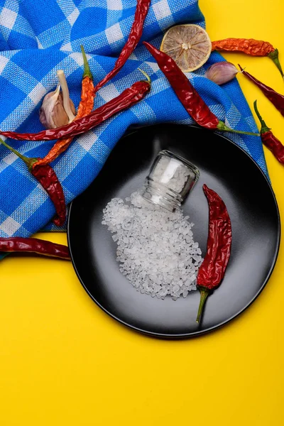 Tarro de vidrio con sal y pimienta roja en plato negro — Foto de Stock