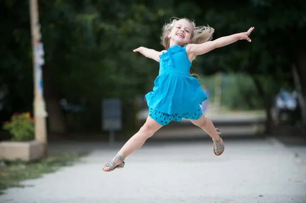 Liten flicka med leende ansikte hoppning i blå klänning — Stockfoto