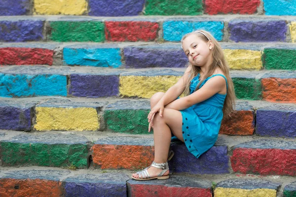 Mała dziewczynka uśmiechający się w niebieskiej sukience na schody kolorowe — Zdjęcie stockowe
