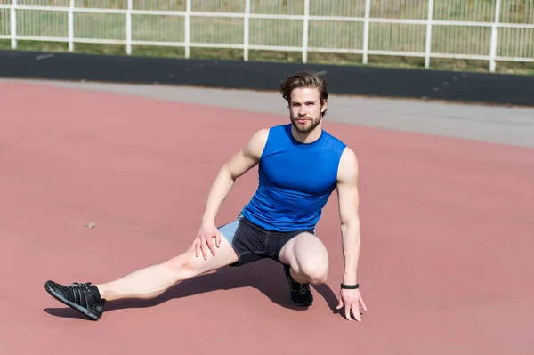 Atlético barbudo hombre con cuerpo muscular estiramiento en pista de atletismo — Foto de Stock