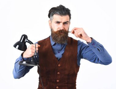 Sakallı adam elinde ciddi yüzüyle masa lambası tutuyor.