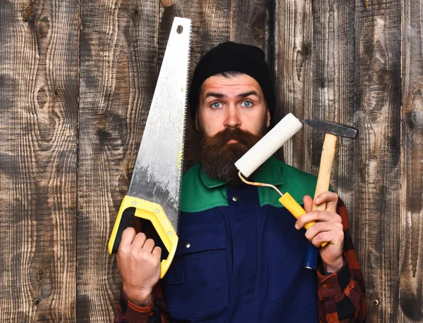 Bärtiger Mann hält mit überraschtem Gesicht verschiedene Bauwerkzeuge in der Hand — Stockfoto