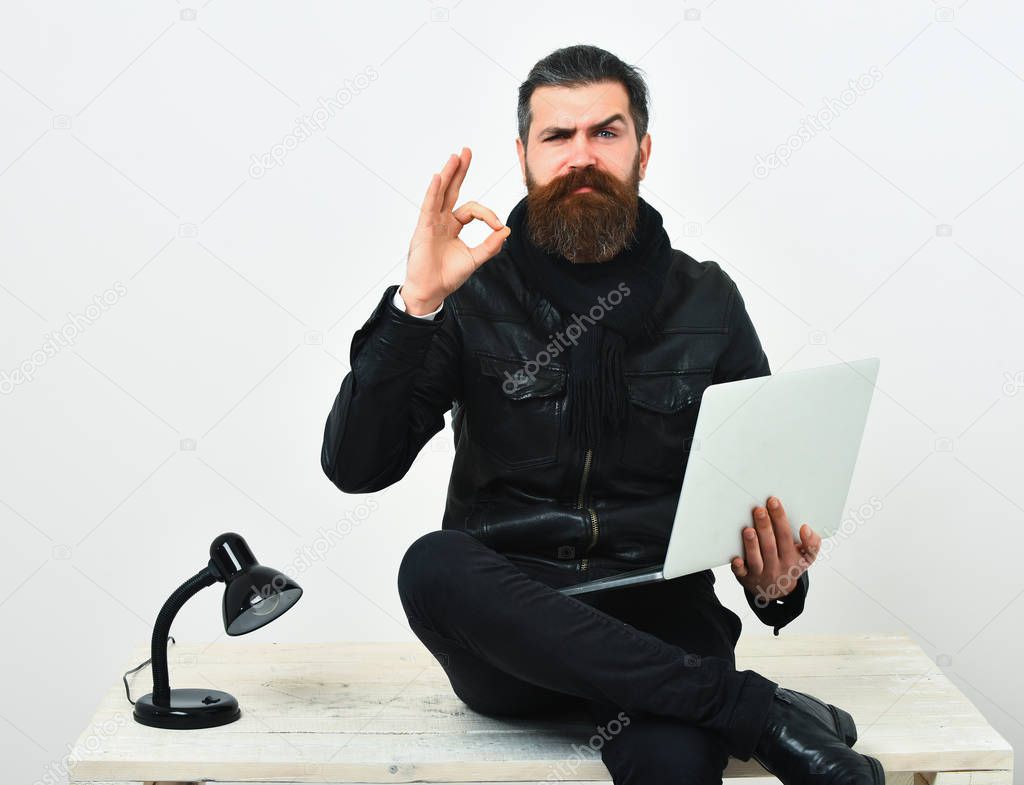 Bearded brutal caucasian hipster sitting on table with laptop