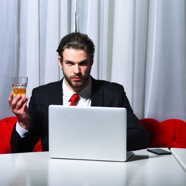 Sakallı adam, elinde bir bardak viski tutan iş adamı dizüstü bilgisayarda çalışıyor.